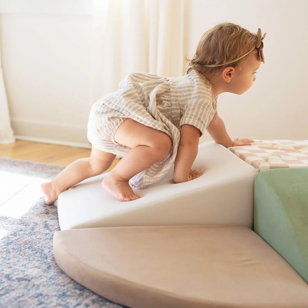 A toddler in a striped dress and headband climbs the Tiny Land® PlayNest Climbing Blocks by Tiny Land INC indoors, with sunlight streaming through a window, building gross motor skills through active play.