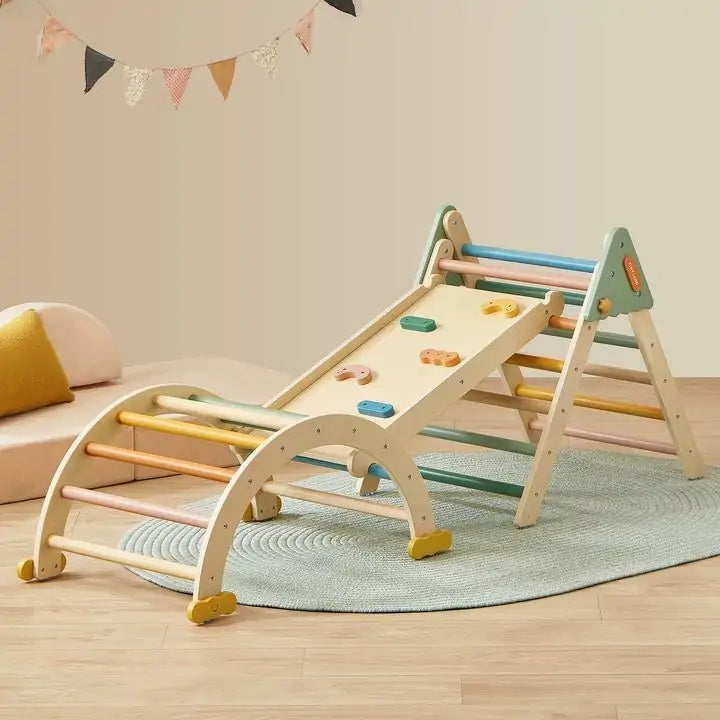 A cozy room showcases the Tiny Land® 7-in-1 Morandi Pikler Triangle Set by Tiny Land, featuring a wooden arch, triangle, slide with handholds, colorful rungs—set atop a round rug with a cushion and festive wall bunting in the background.