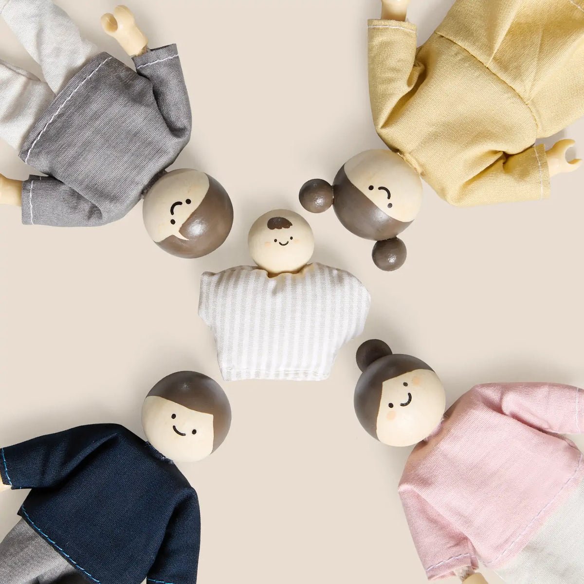 Five Tiny Land® Wooden Dollhouse Dolls by Tiny Land INC, with painted faces and simple clothing in gray, yellow, blue, pink, and striped white, are arranged in a circle on a plain background and viewed from above.
