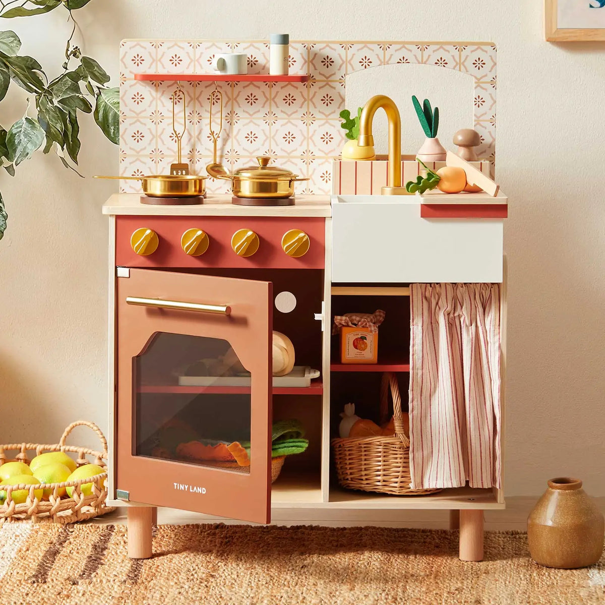 The Tiny Land® Mediterranean Play Kitchen by Tiny Land INC features gold pots, utensils, a sink, play food, faux tile backsplash, glass-door oven, curtain, shelves, and a basket of play fruits.