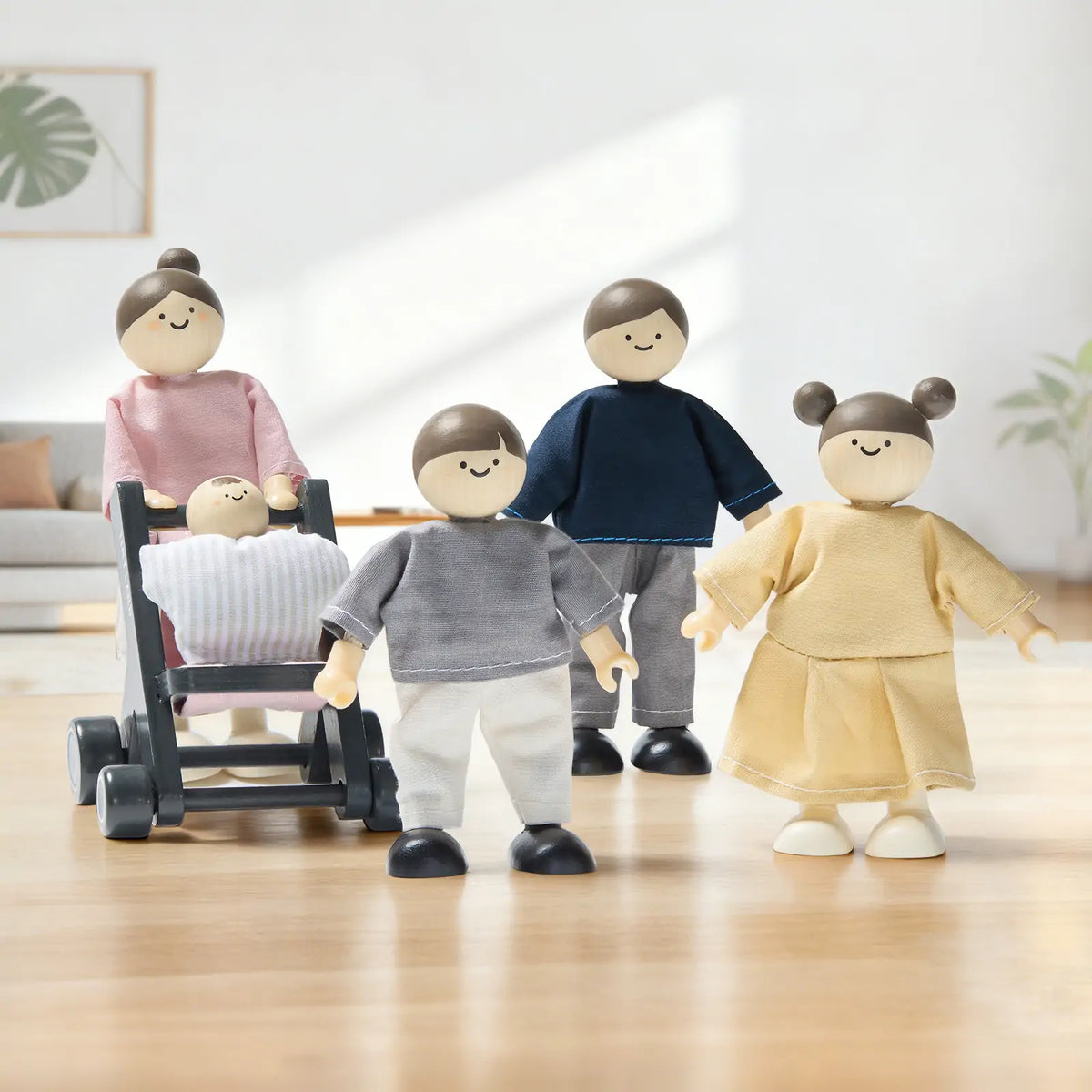 Five Tiny Land® Wooden Dollhouse Dolls by Tiny Land INC, featuring simple painted faces and pastel outfits, stand in a bright room. One poseable wooden doll pushes a stroller with a baby, while three others stand nearby.