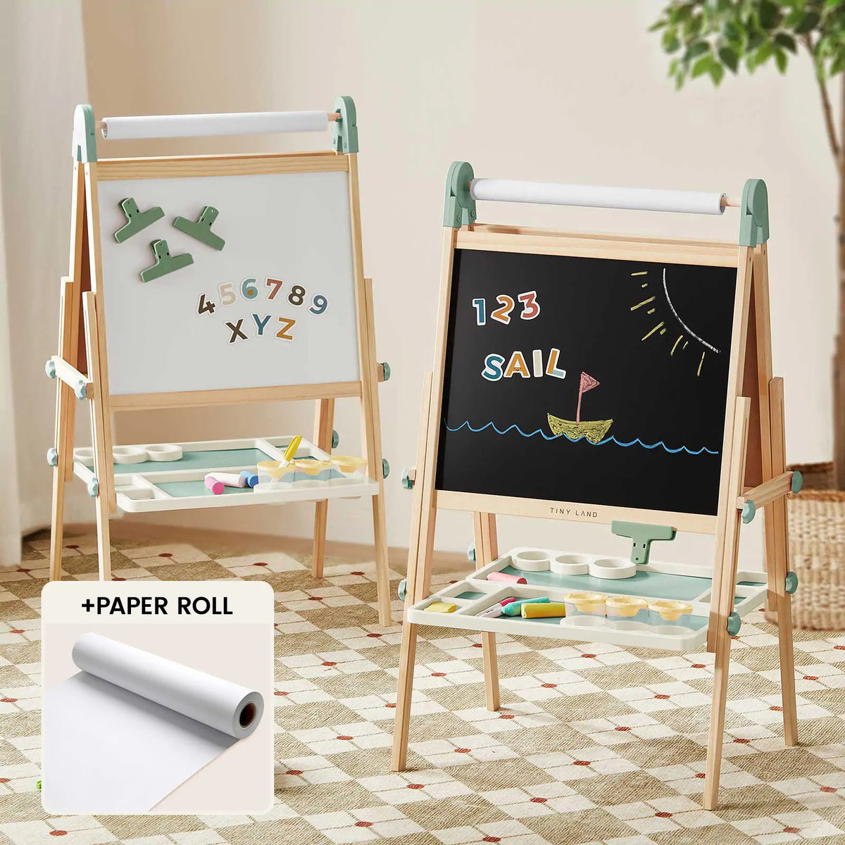 Two Tiny Land® Green Magnitales Easel & Paper Roll Sets stand on a checkered rug; one displays magnets and letters, the other shows “123 SAIL” with a sailboat drawing. An inset highlights Tiny Land’s built-in paper roll holder.