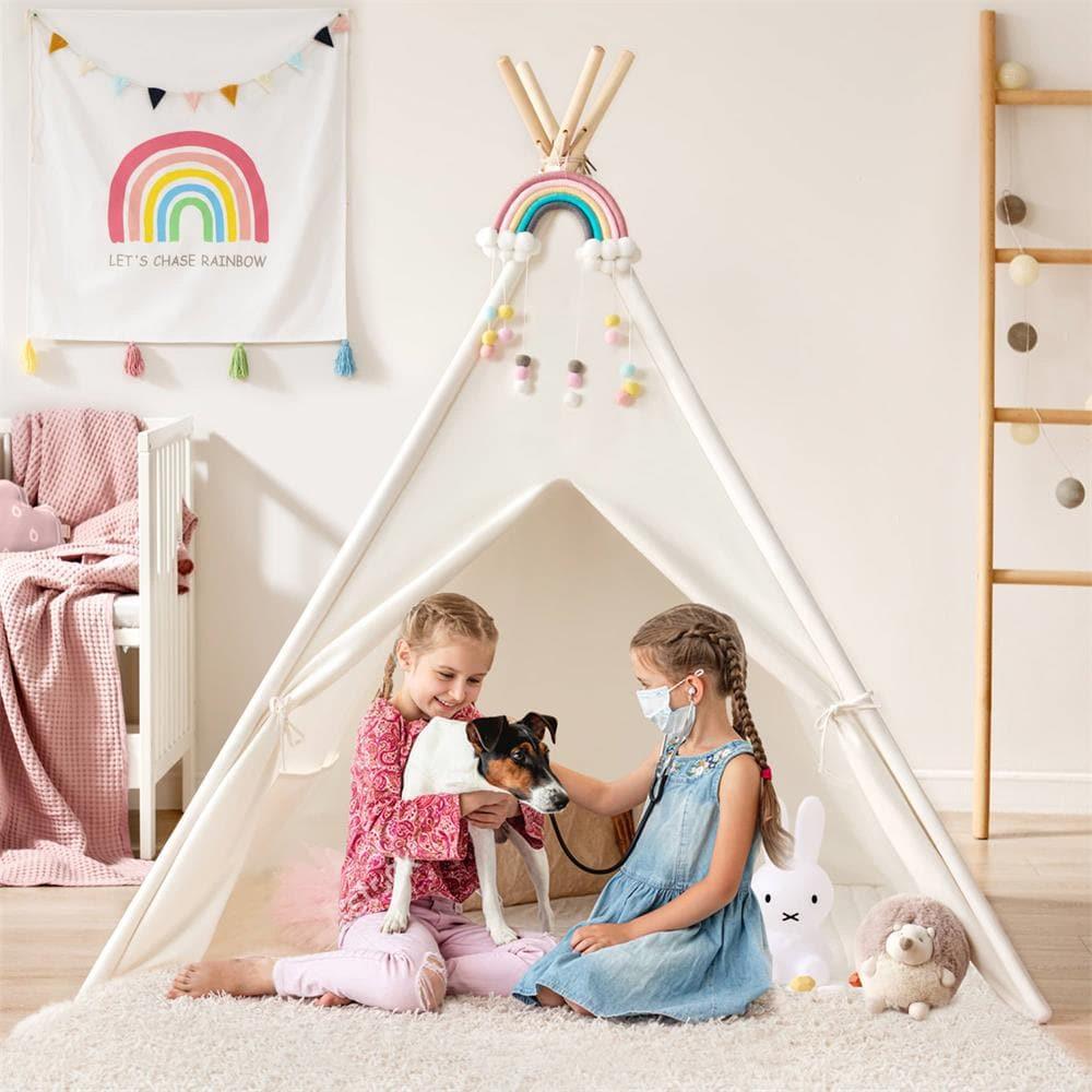 Two young girls play inside the Tiny Land® Teepee Tent for Kids with Mat. One holds a small dog while the other, wearing a toy stethoscope, pretends to give it a checkup. Plush toys and charming Tiny Land decor complete the cozy scene.