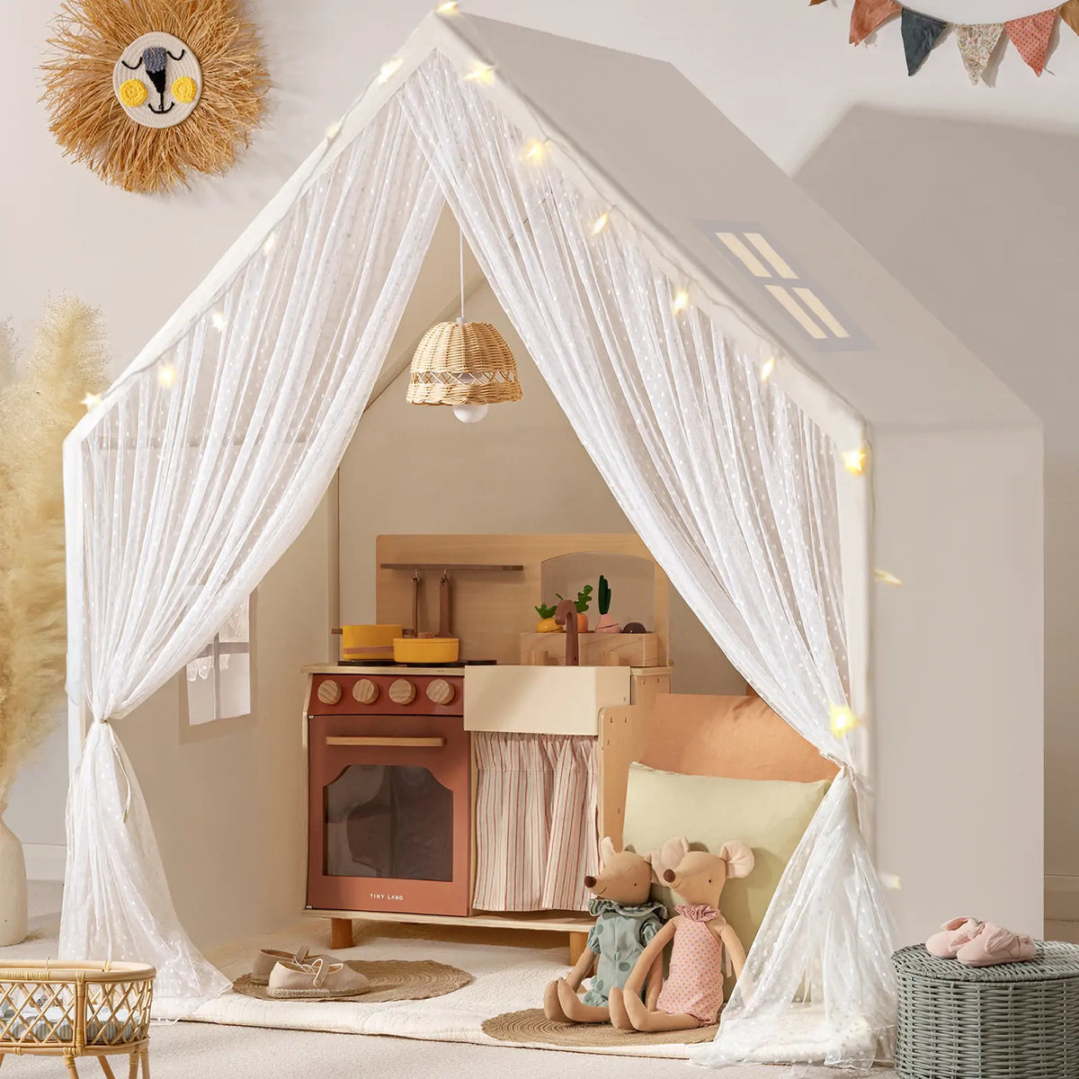 The Tiny Land® Large Space Play House with Star Lights by Tiny Land features white sheer curtains, warm lighting, a toy kitchen, cushions, two plush mice dolls on a round rug, plus decorative bunting and accents on a beige wall.