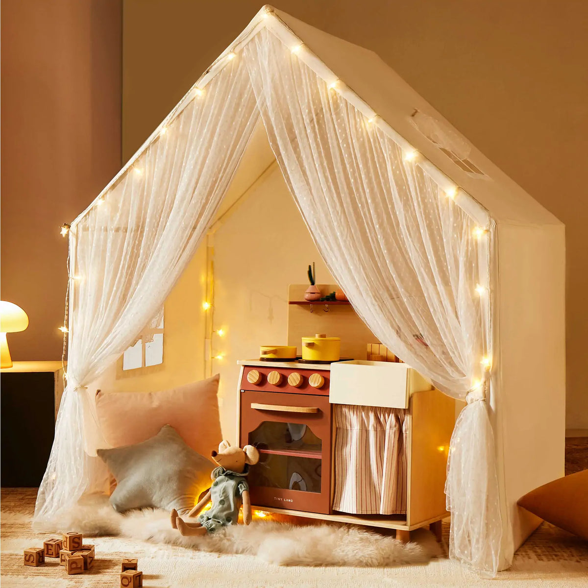 The Tiny Land® Large Space Play House by Tiny Land features star lights, sheer curtains, toy kitchen appliances, plush cushions, a stuffed mouse doll, wooden blocks, and a soft rug for cozy indoor play.